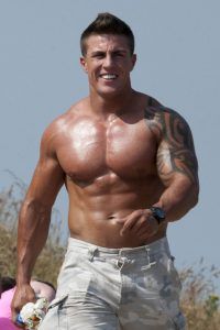 Marc ONeill pictured walking and smiling, he is shirtless and wearing beighe shorts and a black watch.